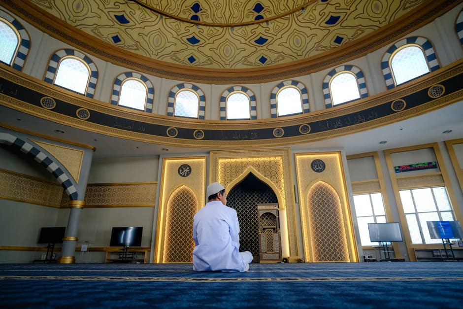 Foto sebuah mushaf Al-Quran tua yang terbuka di atas meja kayu perpustakaan klasik dengan pencahayaan remang yang hangat, dikelilingi oleh tumpukan kitab turats dan naskah kuno, menciptakan suasana keilmuan yang mendalam dan tenang.