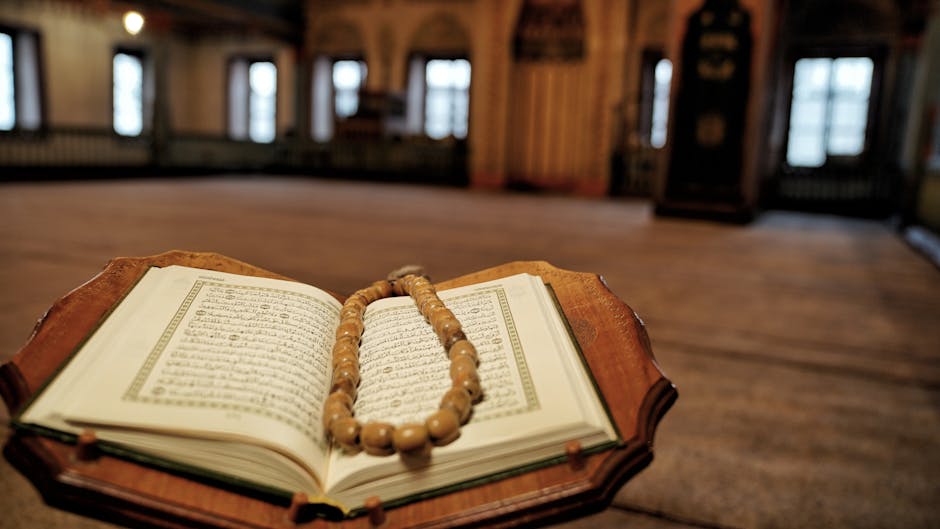 Foto sebuah mushaf Al-Quran yang terbuka di atas meja kayu di dalam perpustakaan klasik dengan cahaya hangat, di sampingnya terdapat naskah tulisan tangan ulama dan tasbih, menciptakan suasana ilmiah dan tenang.