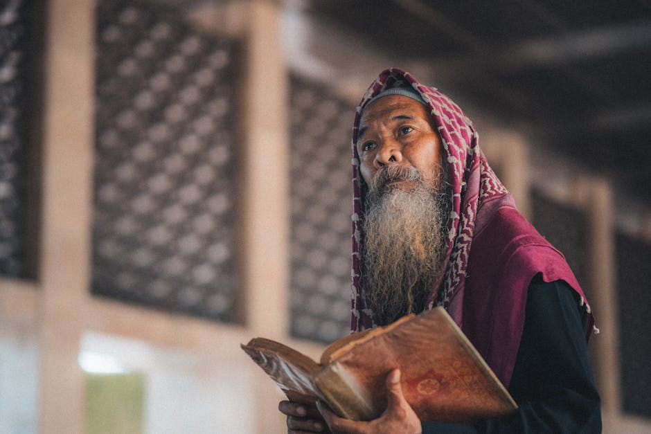 Foto sebuah naskah kitab kuning klasik yang terbuka di atas meja kayu tua dengan pencahayaan hangat dari lampu gantung masjid, menciptakan suasana ilmiah dan religius yang mendalam.
