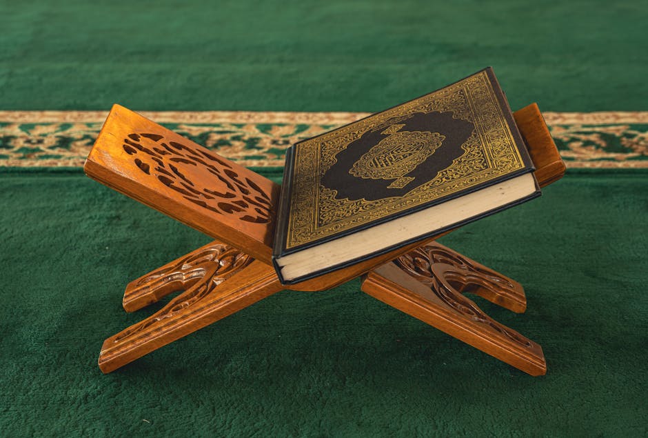 Foto sebuah naskah kitab kuning klasik yang terbuka di atas meja kayu tua dengan pencahayaan hangat dari lampu gantung masjid, menunjukkan kedalaman tradisi keilmuan Islam dalam membahas adab dan doa.