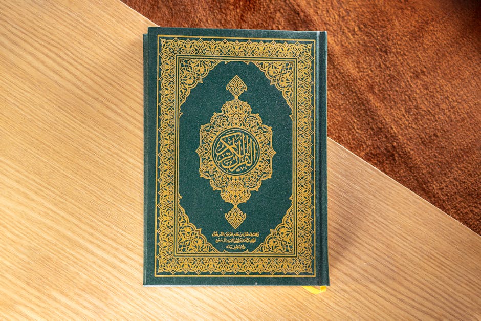 Foto sebuah naskah kuno kitab kuning klasik tentang akidah yang diletakkan di atas meja kayu dengan pencahayaan hangat di dalam perpustakaan pesantren yang penuh dengan deretan kitab-kitab tebal.