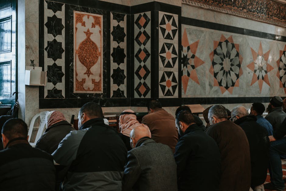 Foto naskah klasik kitab kuning beraliran teologi Asy’ariyyah yang terbuka di atas meja kayu tua dengan pencahayaan hangat, dikelilingi oleh tumpukan kitab-kitab turats di dalam sebuah perpustakaan tradisional Islam yang tenang.