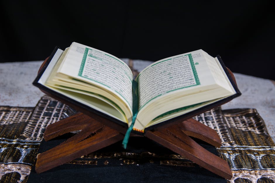 Foto sebuah naskah klasik kitab kuning beraliran Asy'ariyah yang diletakkan di atas meja kayu di dalam perpustakaan masjid dengan pencahayaan hangat yang menonjolkan detail kaligrafi Arab.