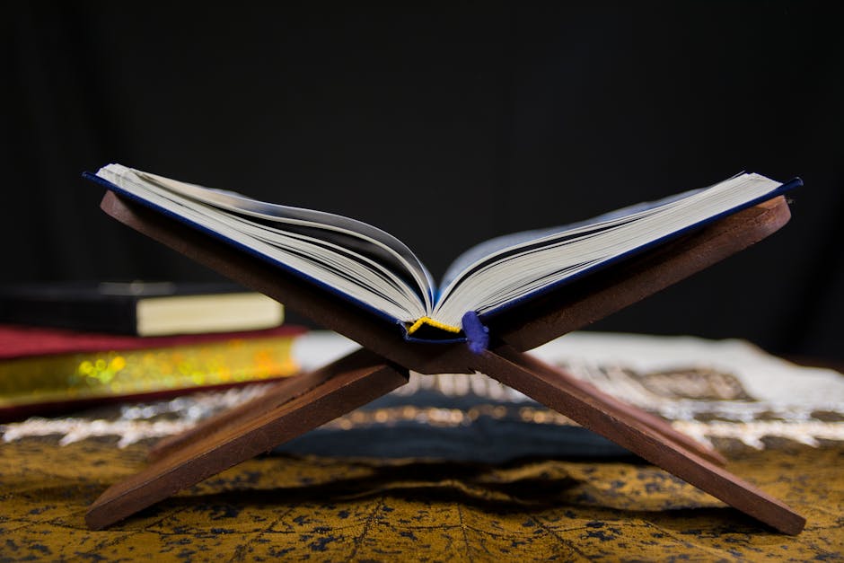 Foto sebuah naskah kuno kitab tauhid dengan tulisan kaligrafi Arab yang indah di atas meja kayu tua, dikelilingi oleh tumpukan kitab kuning di dalam sebuah perpustakaan masjid yang tenang dan bercahaya temaram.