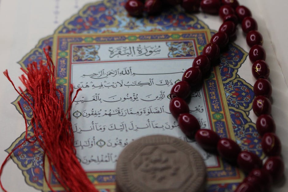 Foto sebuah naskah klasik kitab kuning gundul yang terbuka di atas meja kayu tua dengan pencahayaan hangat dari jendela masjid, menunjukkan kedalaman tradisi literatur Islam dalam membahas ilmu tauhid.