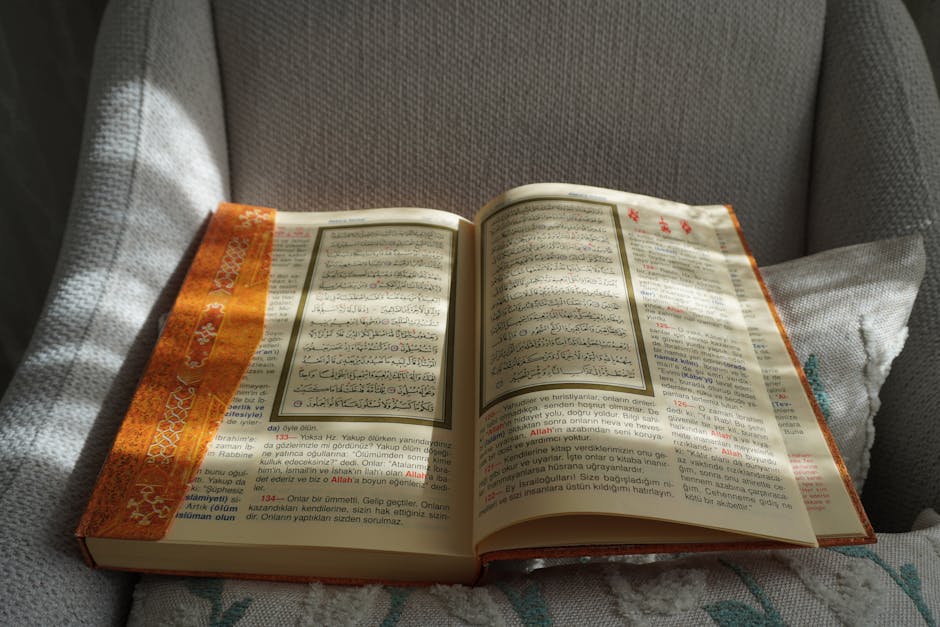 Mushaf Al-Quran yang terbuka di atas meja kayu klasik di dalam sebuah perpustakaan Islam tradisional dengan cahaya matahari lembut yang masuk melalui jendela masjid, menciptakan suasana tenang dan penuh ilmu.