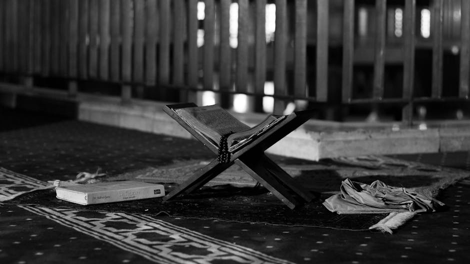 Foto sebuah naskah kitab kuning klasik yang terbuka di atas meja kayu dengan pencahayaan hangat, dikelilingi oleh tumpukan buku-buku referensi akidah di dalam sebuah perpustakaan Islam yang tenang.