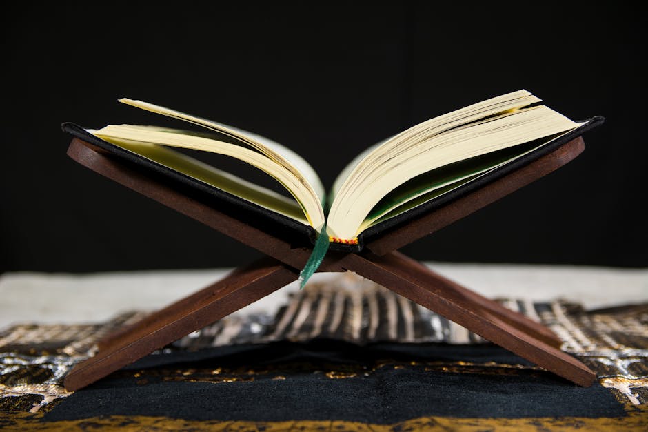 Foto naskah kuno kitab kuning klasik yang terbuka di atas meja kayu jati di sebuah perpustakaan Islam tradisional dengan pencahayaan hangat yang menonjolkan tekstur kertas tua dan tulisan kaligrafi Arab.