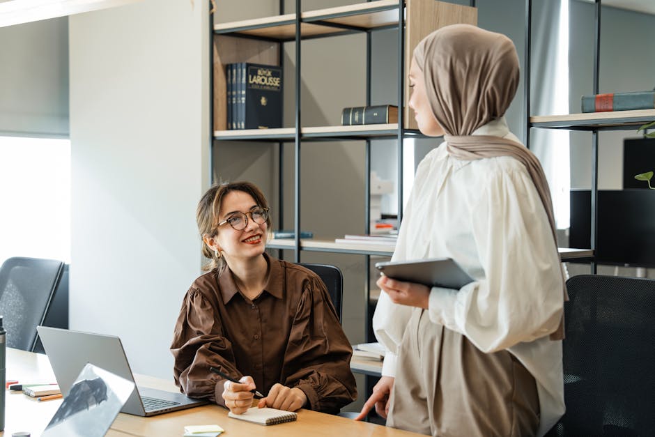 Ilustrasi seorang pemikir Muslim paruh baya yang sedang menulis catatan di meja kayu dengan latar belakang rak buku klasik yang penuh dengan kitab-kitab tebal, menciptakan suasana diskusi ilmiah yang tenang dan mendalam.