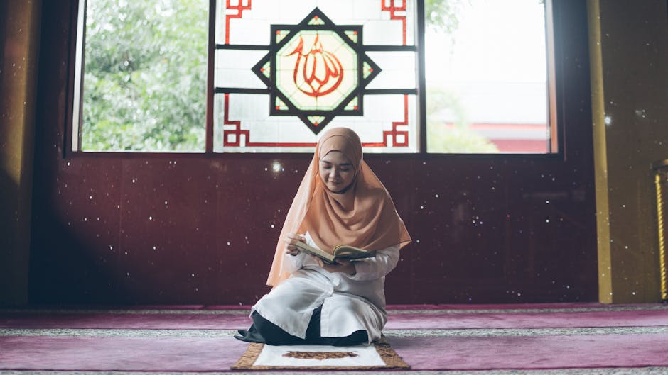 Foto sebuah naskah kitab kuning klasik yang terbuka di atas meja kayu dengan pencahayaan lembut, menunjukkan teks Arab berharakat yang rapi di samping sebuah sajadah di dalam masjid yang tenang.