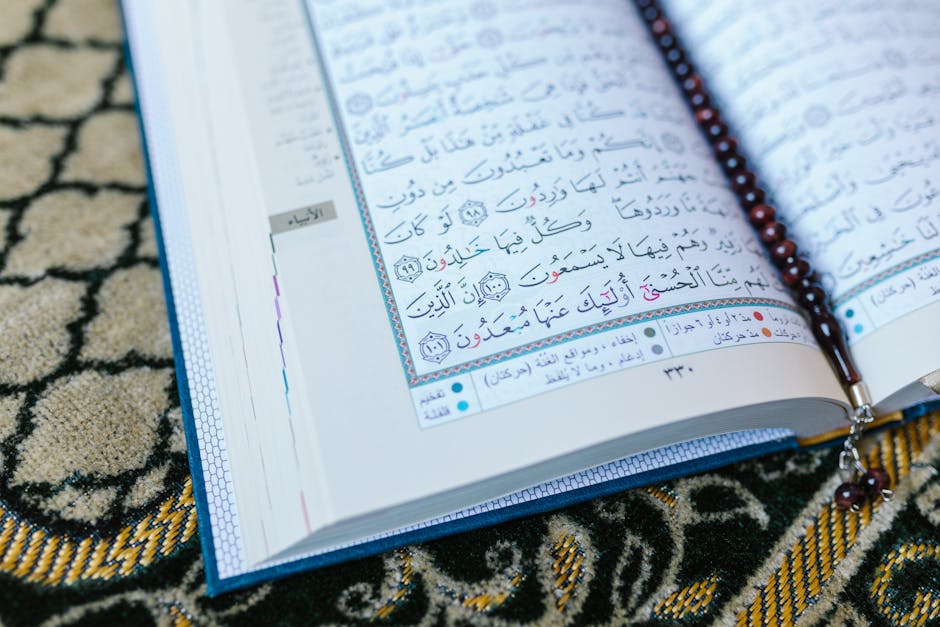 Foto sebuah mushaf Al-Quran yang terbuka di atas meja kayu di dalam perpustakaan klasik dengan latar belakang rak buku kitab kuning yang tersusun rapi, menciptakan suasana ilmiah dan religius yang tenang.