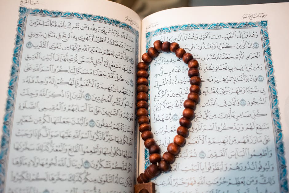 Foto sebuah naskah kuno kitab tafsir dengan tulisan Arab yang indah diletakkan di atas meja kayu jati, di sampingnya terdapat sebuah lampu minyak antik dan latar belakang rak buku perpustakaan Islam yang penuh dengan kitab-kitab klasik bercover kulit.