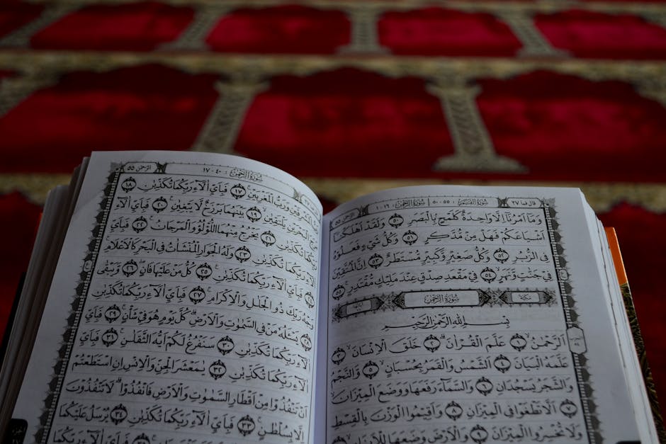 Foto sebuah mushaf Al-Quran tua yang terbuka dengan tulisan kaligrafi yang indah, diletakkan di atas meja kayu di dalam perpustakaan klasik yang dipenuhi buku-buku tebal, menciptakan suasana keilmuan yang mendalam dan tenang.
