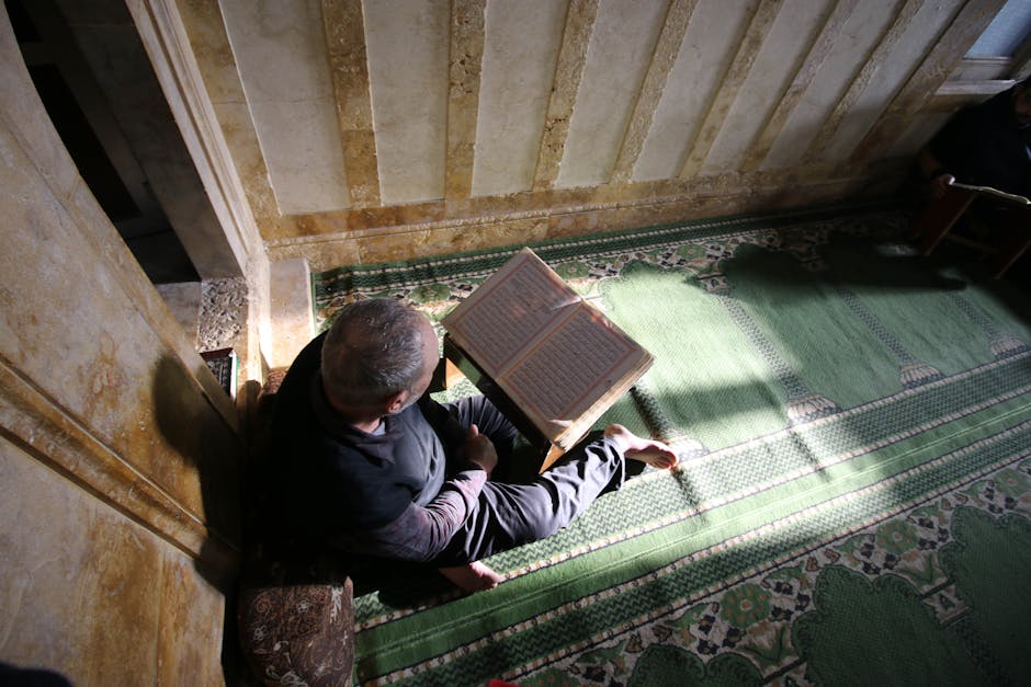 Foto sebuah mushaf Al-Quran yang terbuka di atas meja kayu klasik di dalam sebuah perpustakaan dengan pencahayaan hangat, dikelilingi oleh tumpukan kitab-kitab kuning klasik karya ulama terdahulu.