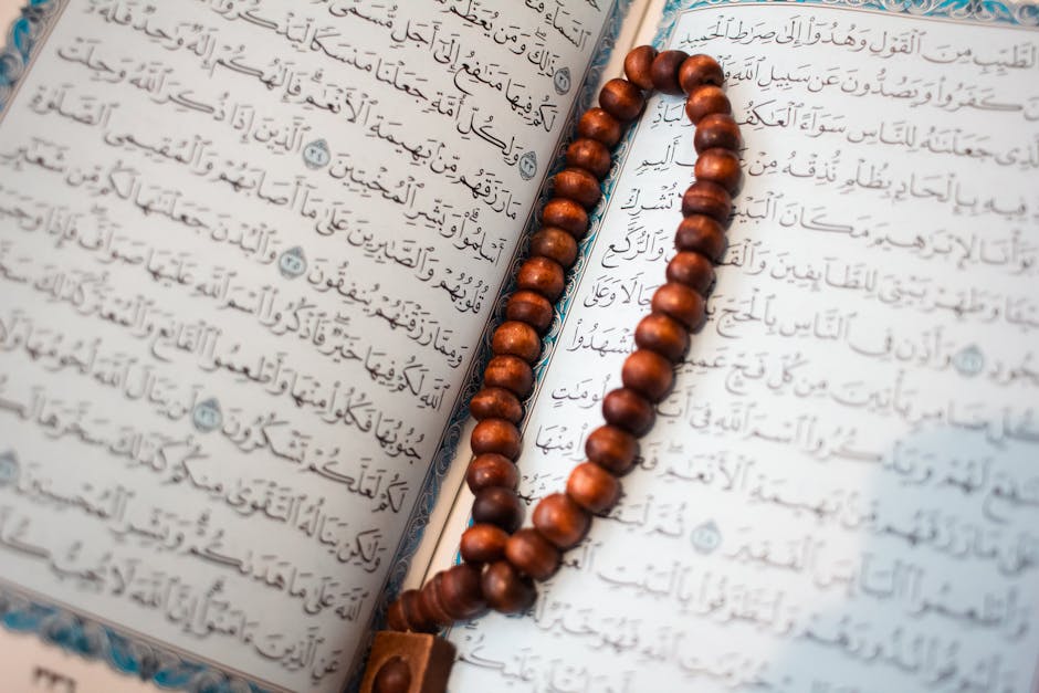 Foto sebuah mushaf Al-Quran kuno dengan tulisan tangan yang indah terbuka di atas meja kayu tua di dalam sebuah perpustakaan klasik yang dipenuhi kitab-kitab kuning, cahaya matahari pagi masuk melalui jendela masjid memberikan kesan sakral dan penuh ilmu.