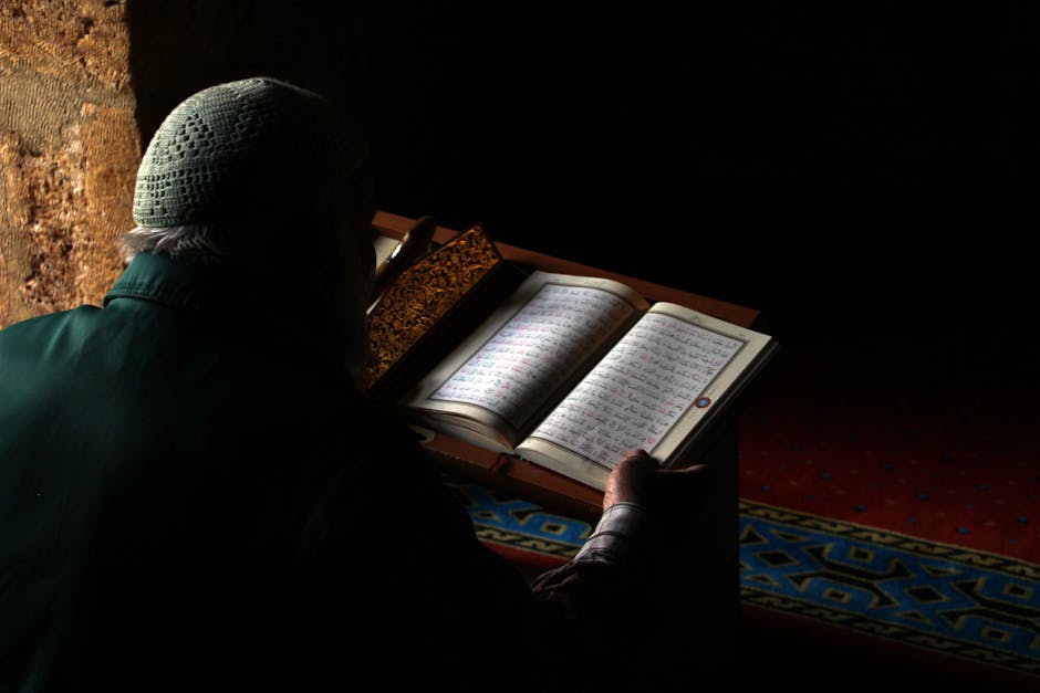 Foto sebuah mushaf Al-Quran kuno dengan tulisan khat yang indah terbuka di atas meja kayu di dalam perpustakaan klasik yang tenang, dengan cahaya matahari pagi yang masuk melalui jendela besar menyinari halaman-halaman kitab tersebut.