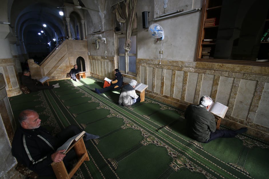 Foto sebuah mushaf Al-Quran tua yang terbuka dengan tulisan kaligrafi yang indah, diletakkan di atas meja kayu di dalam sebuah perpustakaan klasik dengan cahaya hangat yang masuk dari jendela, menciptakan suasana keilmuan yang tenang dan mendalam.