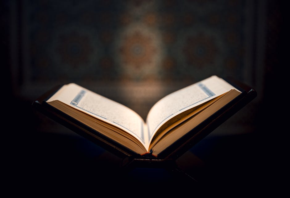 Foto sebuah mushaf Al-Quran terbuka dengan pencahayaan lembut di dalam sebuah perpustakaan klasik yang dipenuhi kitab-kitab kuning, menciptakan suasana keilmuan yang tenang dan berwibawa.