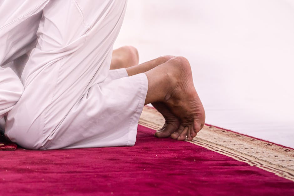 Foto sebuah mushaf Al-Quran tua yang terbuka di atas meja kayu di dalam perpustakaan klasik yang dipenuhi kitab-kitab kuning, dengan cahaya matahari pagi yang masuk melalui jendela masjid, menciptakan suasana tenang dan penuh ilmu.