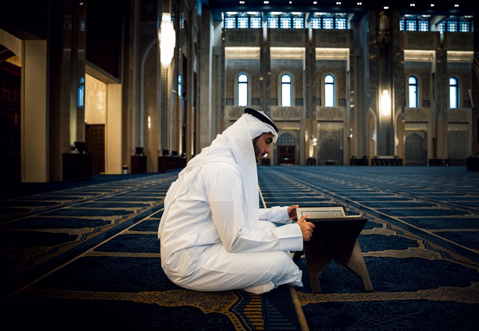 Foto sebuah mushaf Al-Quran terbuka dengan pencahayaan hangat di atas meja kayu perpustakaan klasik yang dipenuhi deretan kitab-kitab turats, melambangkan kedalaman ilmu dan tradisi intelektual Islam.