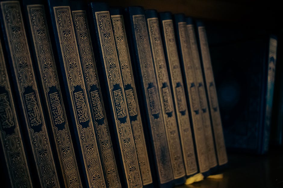 Foto sebuah mushaf Al-Quran terbuka di atas meja kayu klasik di dalam perpustakaan dengan pencahayaan hangat, dikelilingi oleh tumpukan kitab-kitab turats yang melambangkan kedalaman ilmu pengetahuan Islam.