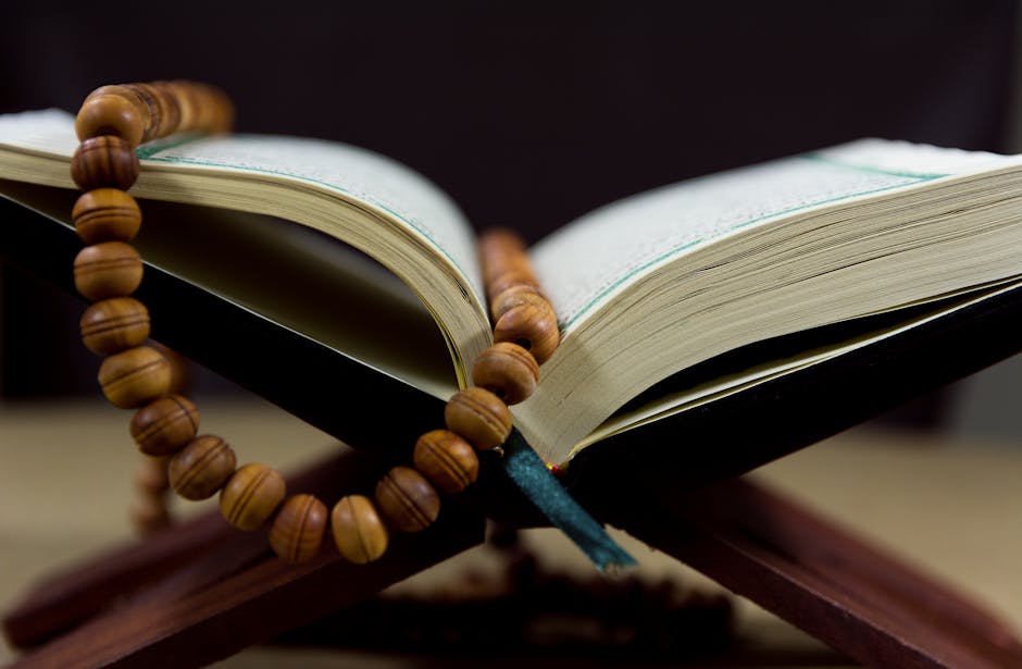 Foto sebuah mushaf Al-Quran terbuka dengan pencahayaan hangat di atas meja kayu perpustakaan klasik, dikelilingi oleh tumpukan kitab-kitab turats yang melambangkan kedalaman ilmu dan tradisi intelektual Islam yang kokoh.