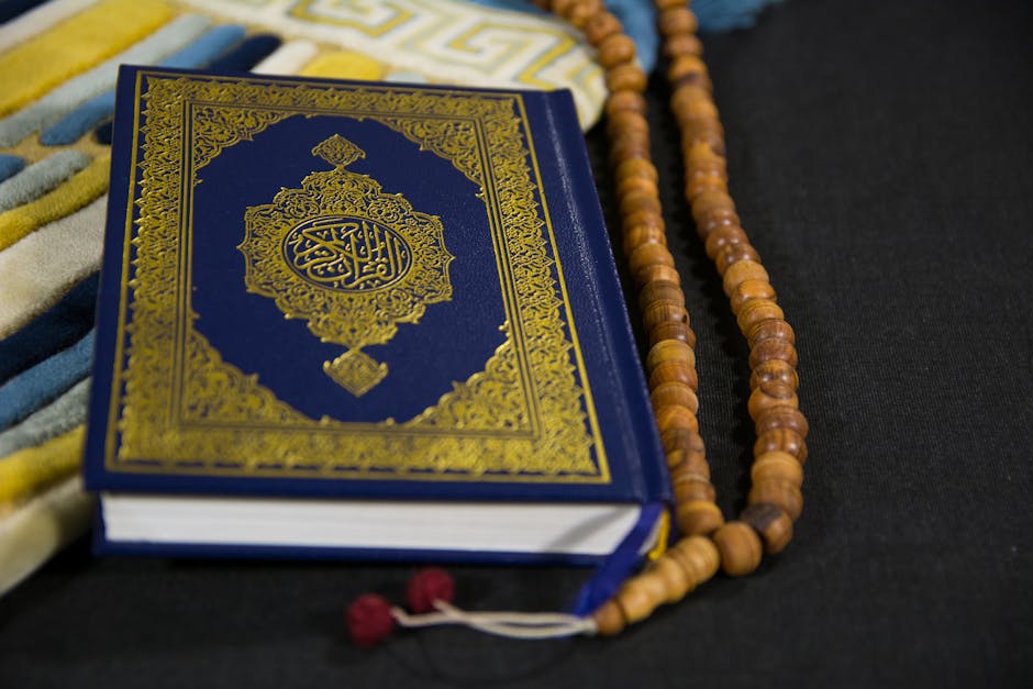 Foto sebuah mushaf Al-Quran yang terbuka dengan pencahayaan hangat di atas meja kayu perpustakaan klasik, dikelilingi oleh tumpukan kitab-kitab kuning referensi ulama terdahulu, menciptakan suasana keilmuan yang tenang dan berwibawa.