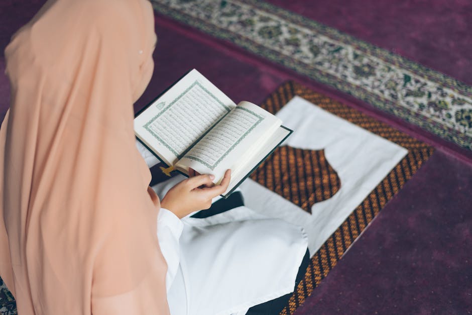 Foto sebuah mushaf Al-Quran terbuka di atas meja kayu di dalam perpustakaan klasik dengan latar belakang rak buku keagamaan yang tersusun rapi dan pencahayaan lampu kuning yang hangat memberikan kesan mendalam dan tenang.