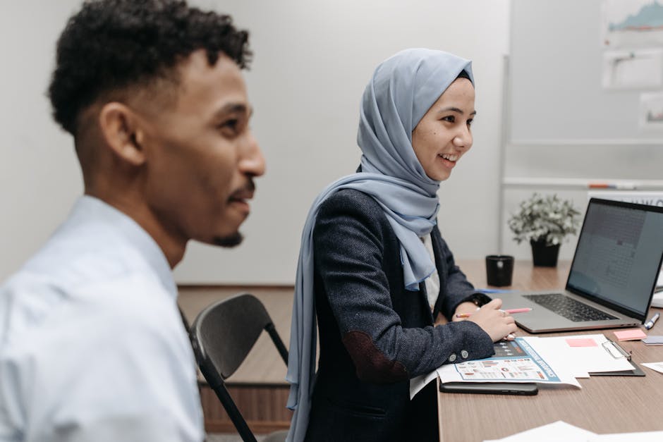 Ilustrasi seorang Muslimah yang sedang menulis di meja kerja dengan latar belakang perpustakaan dan jendela yang menampilkan pemandangan kota modern, melambangkan perpaduan ilmu pengetahuan dan peran sosial.
