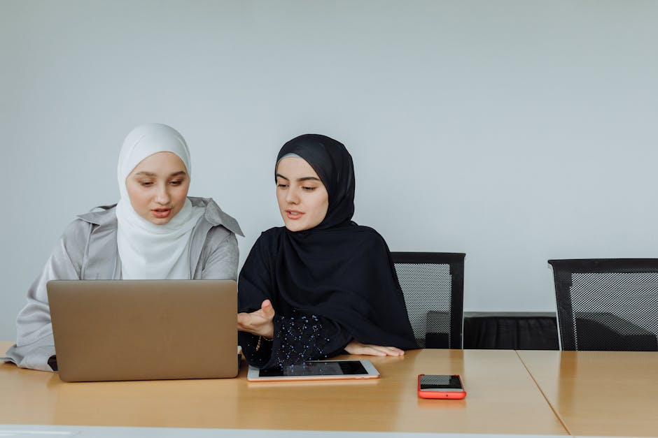 Ilustrasi seorang Muslimah terpelajar yang sedang menulis di meja kerja dengan latar belakang perpustakaan dan jendela yang menampilkan siluet pemandangan kota modern, melambangkan perpaduan antara ilmu pengetahuan tradisional dan kemajuan zaman.