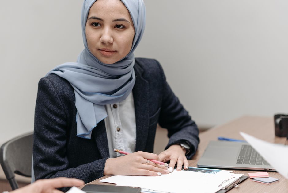Ilustrasi seorang Muslimah sedang membaca buku ilmiah di perpustakaan klasik dengan latar belakang kaligrafi Arab yang anggun, melambangkan perpaduan ilmu pengetahuan modern dan spiritualitas Islam.