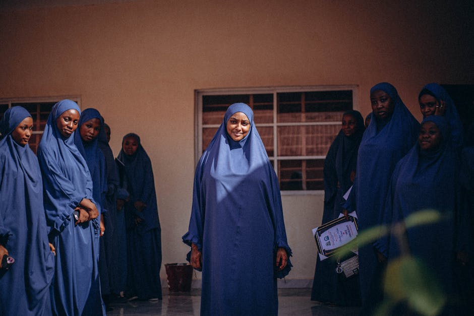 Seorang pemuda Muslim sedang duduk santai di sebuah coffee shop yang estetik dengan pencahayaan hangat, ia sedang melihat ke arah jendela sambil tersenyum tenang, dengan sebuah buku dan segelas kopi di atas meja kayu.