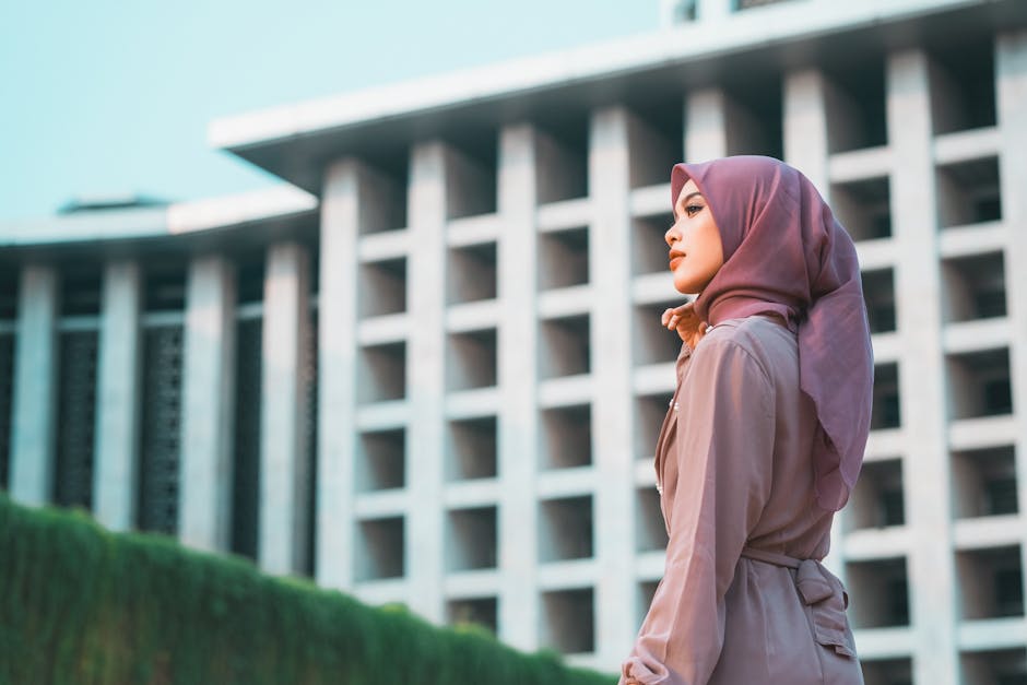 Seorang pemuda Muslim modern menggunakan headphone dan membawa tablet, duduk santai di sebuah taman kota yang estetik dengan latar belakang gedung-gedung modern, menunjukkan perpaduan antara gaya hidup urban dan ketenangan batin.