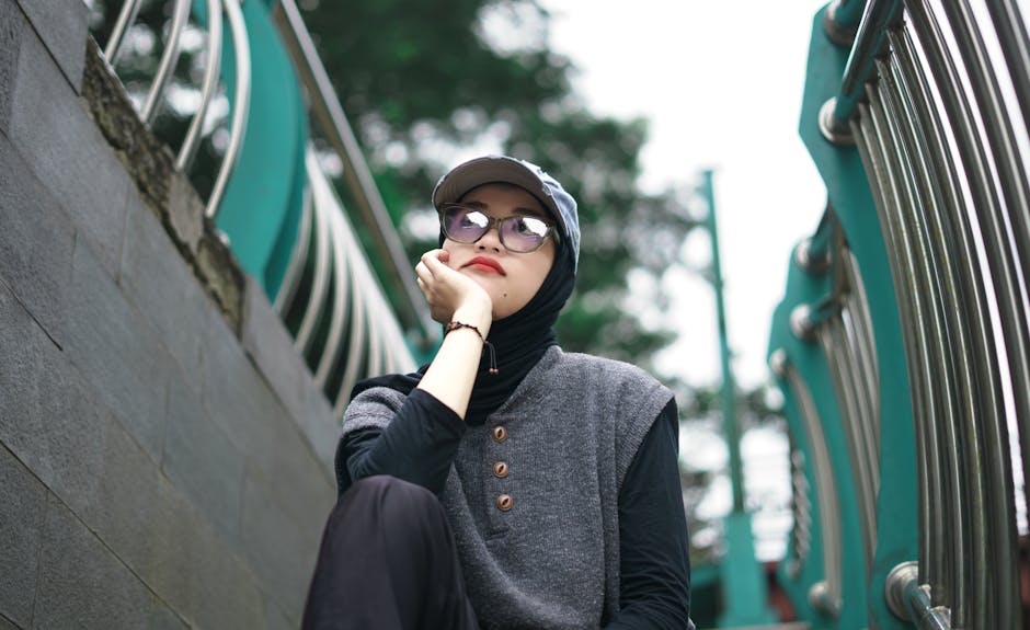 Seorang pemuda Muslim mengenakan hoodie modern sedang duduk santai di sebuah taman kota yang estetik sambil memegang buku catatan, wajahnya tampak tenang sambil menatap senja, menggambarkan suasana refleksi diri yang positif.