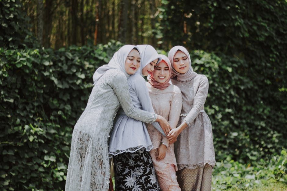 Seorang pemuda Muslim mengenakan hoodie modern dan headphone di leher, sedang duduk santai di taman kota yang hijau sambil memegang buku catatan dan tersenyum melihat pemandangan, mencerminkan ketenangan di tengah hiruk-pikuk perkotaan.