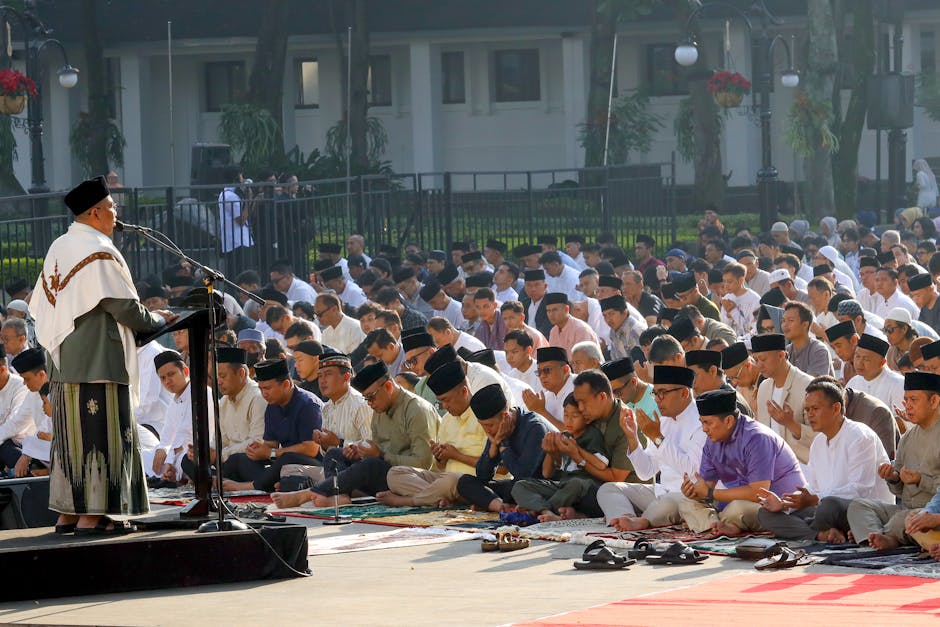 Foto estetik seorang pemuda Muslim sedang duduk santai di taman kota yang modern sambil memegang buku dan secangkir kopi, terlihat tenang dan damai dengan pemandangan gedung-gedung tinggi di latar belakang yang sedikit blur.