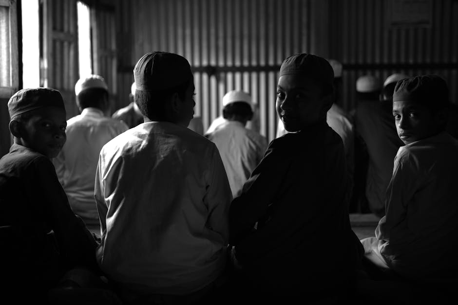 Seorang pemuda Muslim mengenakan hoodie modern dan sneakers sedang duduk santai di sebuah coffee shop estetik, memegang segelas kopi sambil tersenyum menatap ke arah jendela dengan tenang, di latar belakang terdapat suasana kafe yang minimalis dan nyaman.