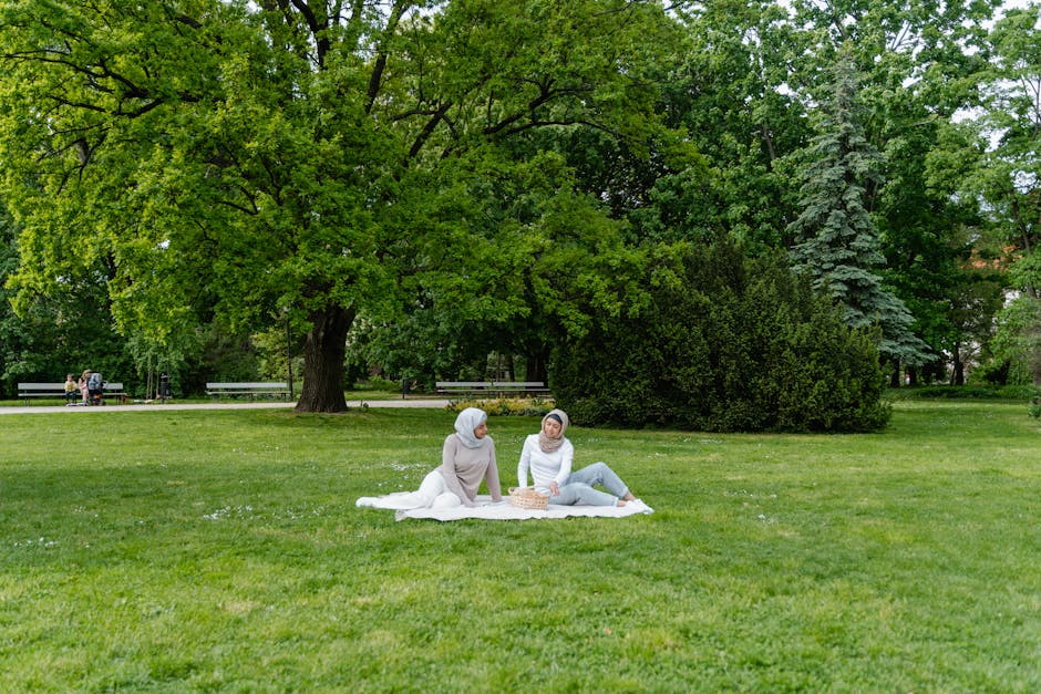 Seorang pemuda Muslim mengenakan hoodie modern sedang duduk santai di sebuah taman kota yang asri sambil memegang buku catatan, wajahnya tampak tenang dan damai dengan latar belakang gedung-gedung perkotaan yang estetik saat matahari terbenam.