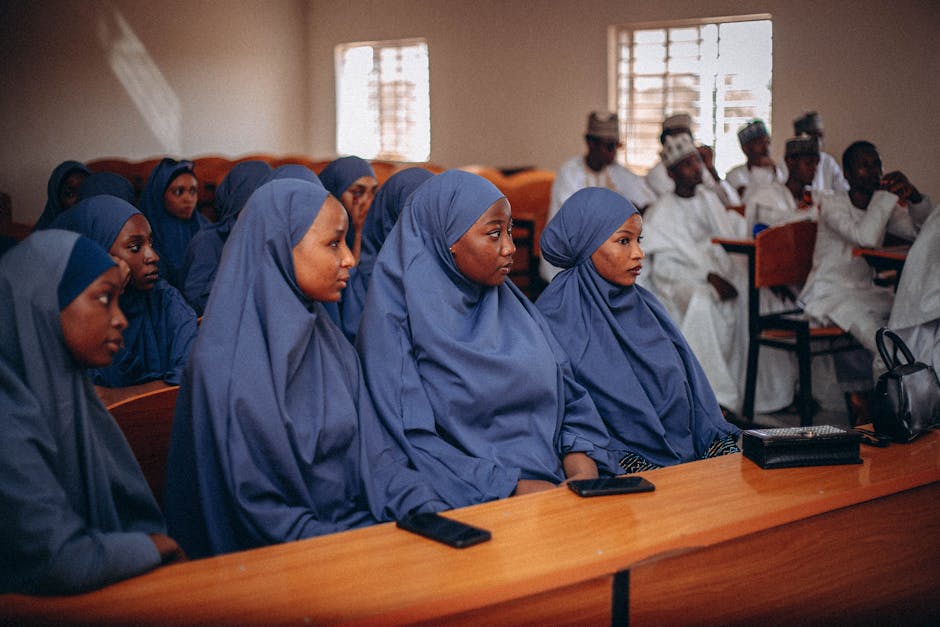 Seorang pemuda Muslim mengenakan hoodie modern dan headphone di leher, sedang duduk tenang di kursi taman kota yang asri sambil melihat pemandangan langit sore yang damai, menunjukkan ekspresi wajah yang tenang dan reflektif.