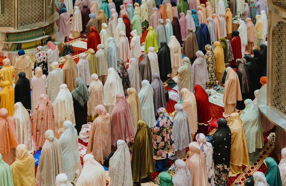 Seorang pemuda Muslim mengenakan hoodie modern dan sneakers sedang duduk santai di area taman kota yang estetik sambil memegang buku catatan, dengan latar belakang gedung perkantoran modern di sore hari yang cerah.