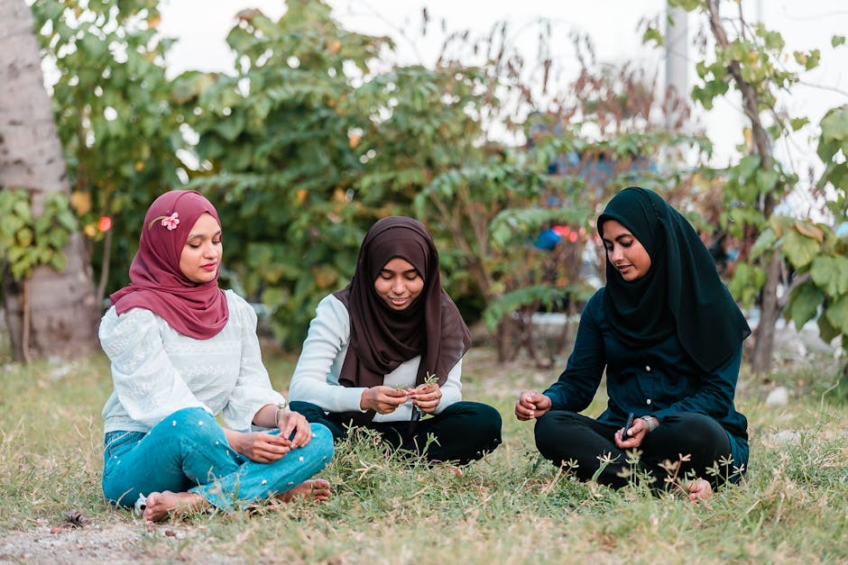 Seorang pemuda Muslim mengenakan hoodie modern sedang duduk santai di sebuah taman kota yang estetik, memegang buku catatan dan terlihat tenang sambil menatap pemandangan, mencerminkan suasana refleksi diri dan ketenangan batin.