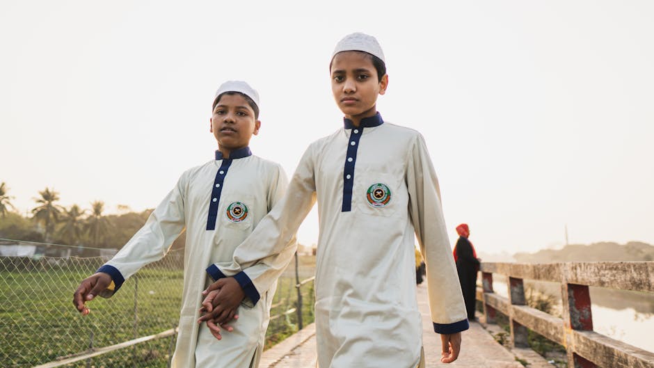 Seorang pemuda Muslim mengenakan hoodie modern sedang duduk santai di taman kota sambil memegang buku, terlihat tenang dengan pemandangan kota yang sibuk di latar belakangnya.