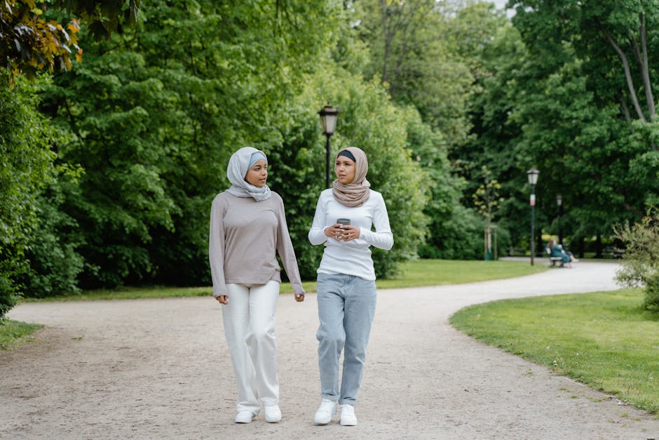 Seorang pemuda Muslim mengenakan hoodie modern dan tas ransel sedang duduk santai di sebuah kafe minimalis, sambil memegang buku catatan dan tersenyum tenang menatap jendela yang cerah.