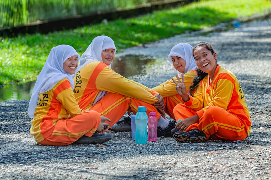 Deskripsi gambar dalam Bahasa Indonesia: Seorang pemuda Muslim mengenakan hoodie modern dan tas punggung sedang duduk santai di sebuah taman kota yang asri sambil memandang matahari terbenam dengan ekspresi wajah yang tenang dan damai.