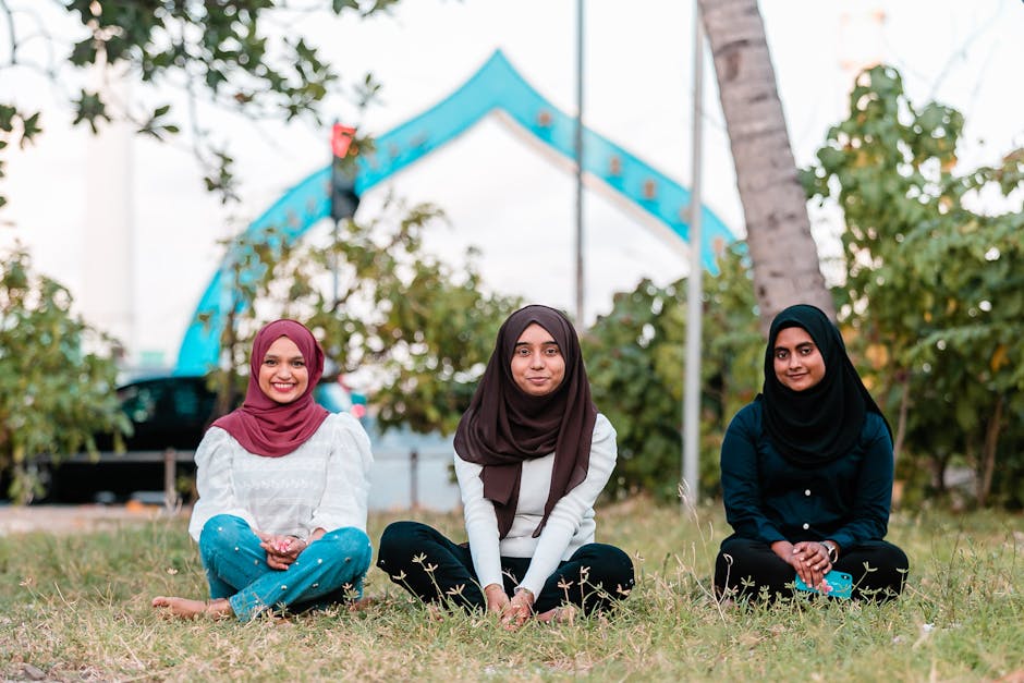 Seorang pemuda Muslim mengenakan hoodie modern sedang duduk santai di taman kota sambil memegang buku dan tersenyum tenang, dengan latar belakang gedung-gedung perkotaan yang agak blur untuk menunjukkan suasana kedamaian di tengah hiruk pikuk kota.