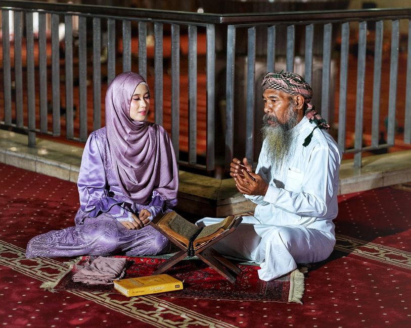 Foto estetik dari sudut pandang atas yang memperlihatkan seorang pemuda Muslim sedang duduk santai di sudut kafe modern yang minimalis, sedang membaca buku dengan segelas kopi hangat di mejanya, menciptakan suasana tenang dan reflektif.
