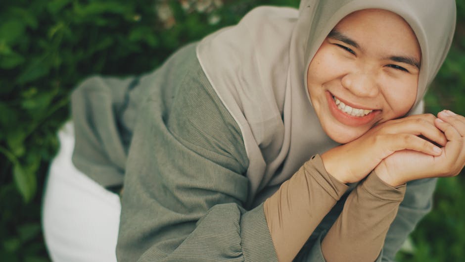 Dua orang pemuda Muslim modern sedang duduk santai di sudut kafe estetik yang dipenuhi tanaman hijau, salah satunya sedang memegang kopi hangat sambil tersenyum mendengarkan temannya bercerita, menciptakan suasana diskusi yang hangat dan menenangkan.