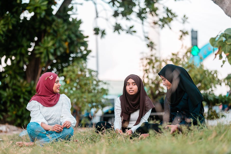 Foto estetik seorang pemuda Muslim mengenakan pakaian kasual modern sedang duduk santai di sudut kafe minimalis, memegang cangkir kopi hangat sambil tersenyum menatap layar ponselnya dengan ekspresi tenang dan damai.