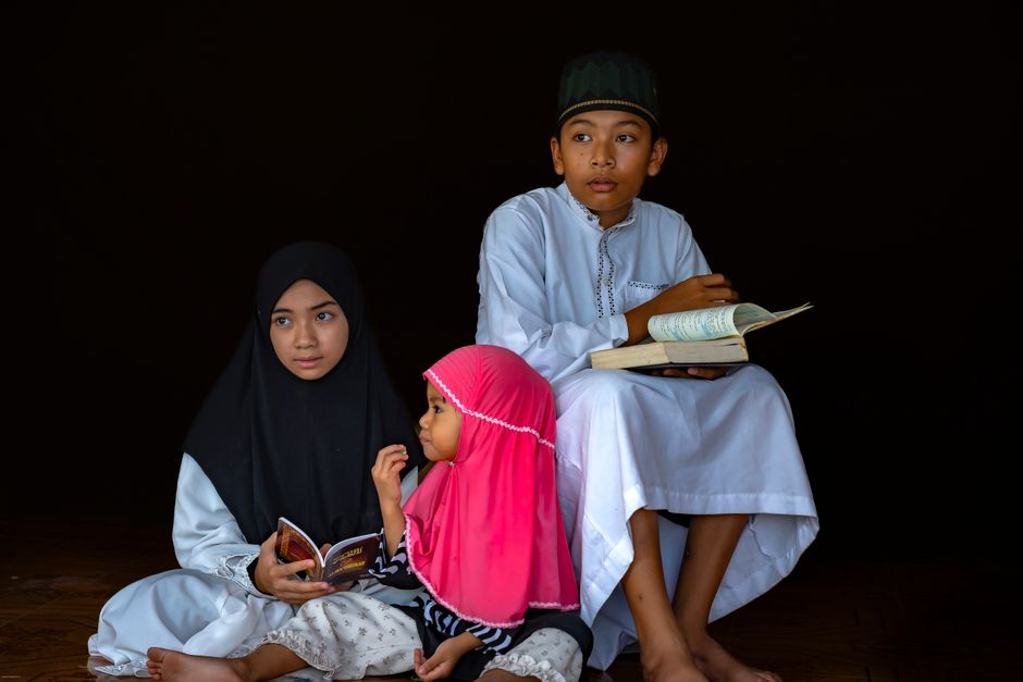 Seorang pemuda Muslim modern sedang duduk santai di sudut kafe estetik sambil memegang secangkir kopi hangat dan melihat layar ponselnya dengan senyum tenang, mengenakan jaket kasual dan jam tangan pintar.