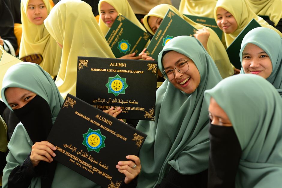 Ilustrasi anak muda Muslim modern yang sedang duduk santai di sudut kafe estetik sambil memegang secangkir kopi hangat, dengan laptop terbuka di meja, menampilkan ekspresi wajah yang tenang dan damai setelah meletakkan smartphone-nya.
